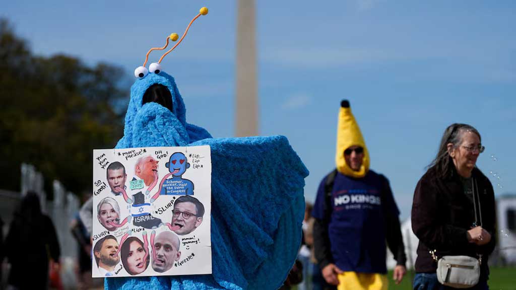 ওয়াশিংটন ডিসির এক বিক্ষোভকারীর পরনে কল্পিত এক চরিত্রের কস্টিউম, হাতে রিপাবলিকান শীর্ষ নেতাদের ইসরায়েলের দালাল আখ্যায়িত করা প্ল্যাকার্ড। ছবি: রয়টার্স