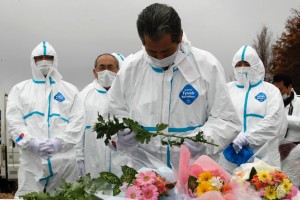 Evacuees dressed in protective suits offer flowers and prayers for victims on the anniversary of Japan Tsunami. Photo: Reuters 